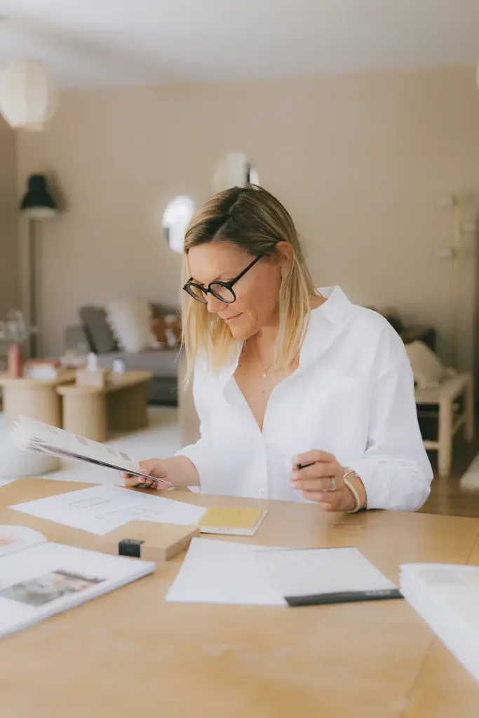Amandine Ferreira à sa table de travail, un nuancier de couleurs à la main, des plans et des échantillons devant elle
