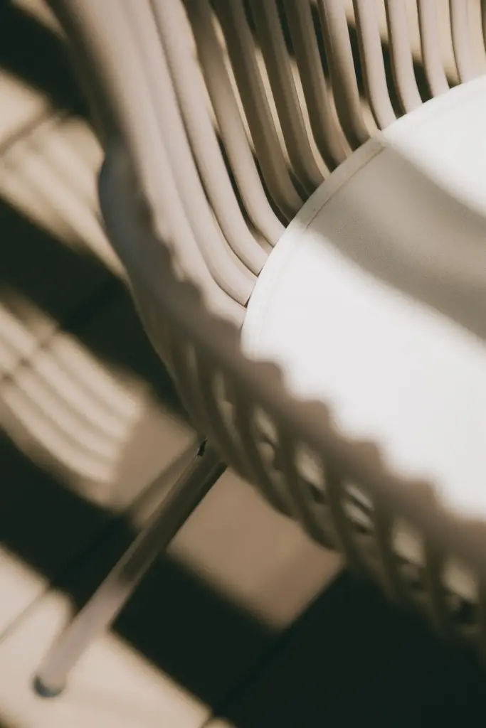 Dossier d’une chaise en corde beige et son coussin blanc, traversés par l’ombre et le soleil