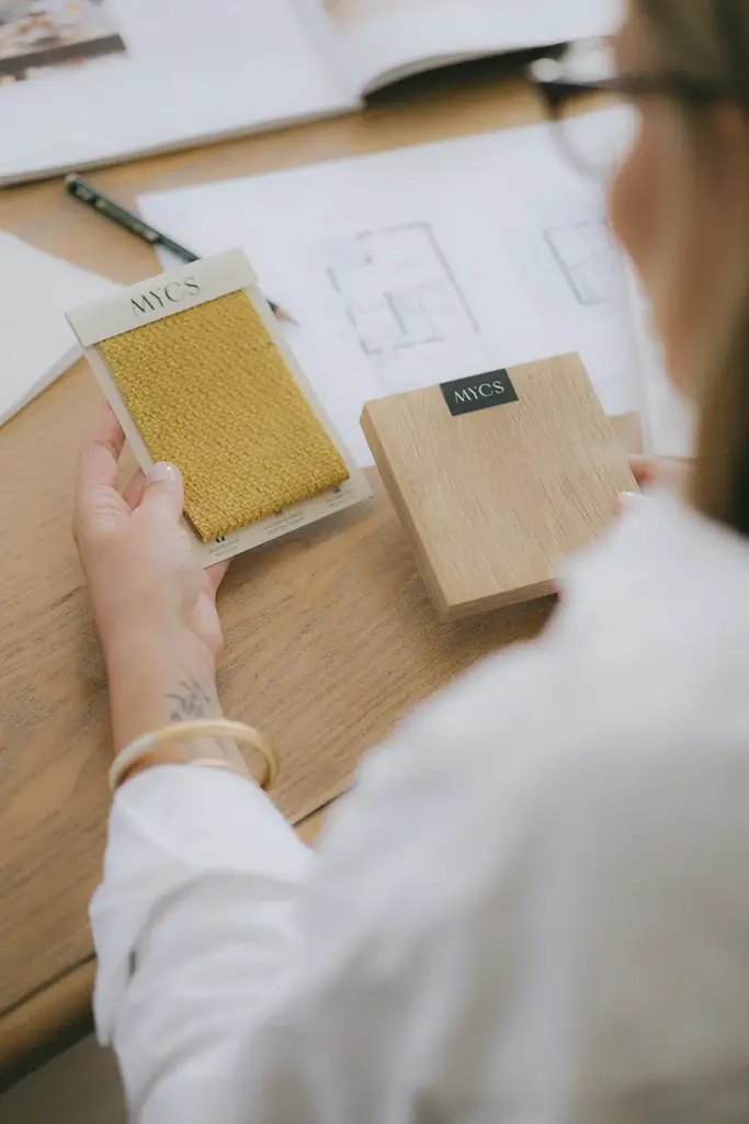 Échantillons de bois et de tissu posés sur des plans d’aménagement, vus par-dessus l’épaule