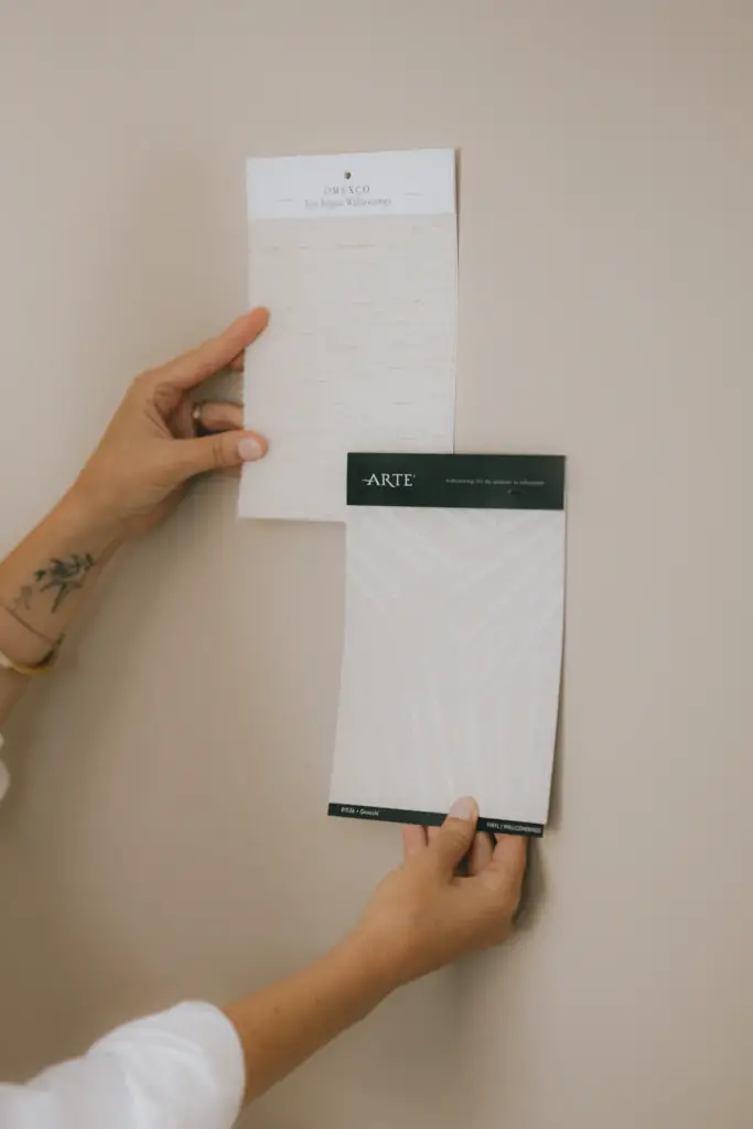 Mains tenant des échantillons de papier peint contre un mur pour juger la couleur à la lumière du jour