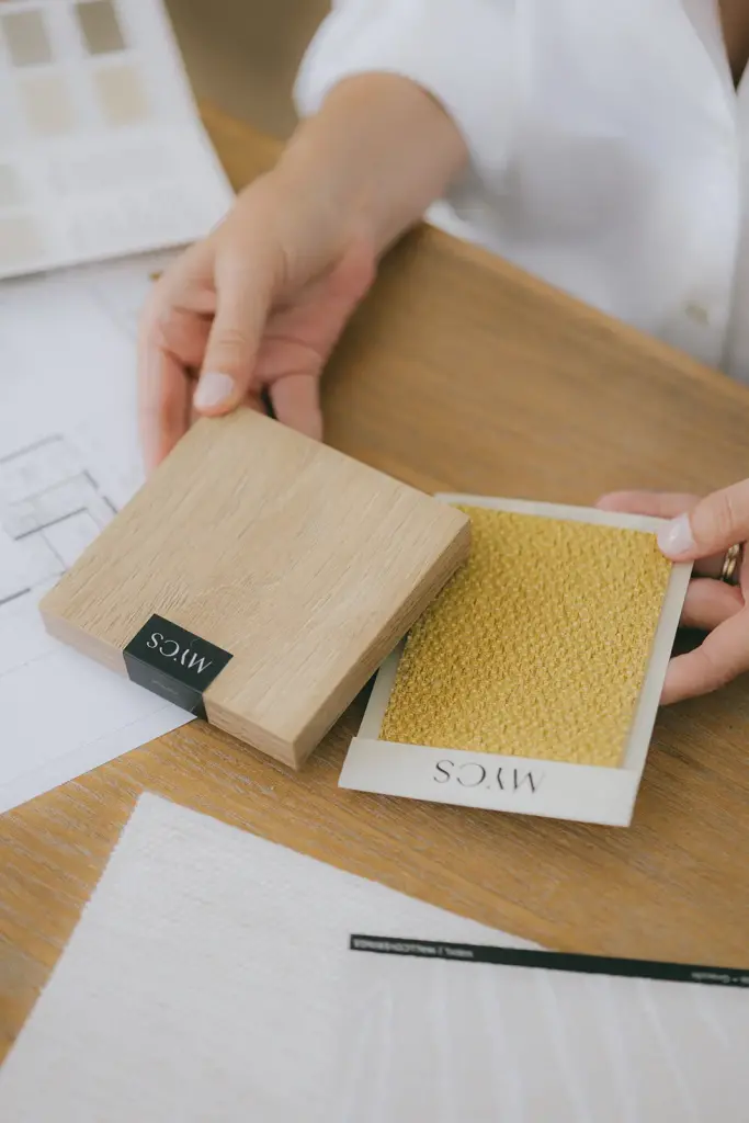 Mains tenant un échantillon de chêne et un tissu moutarde au-dessus des plans