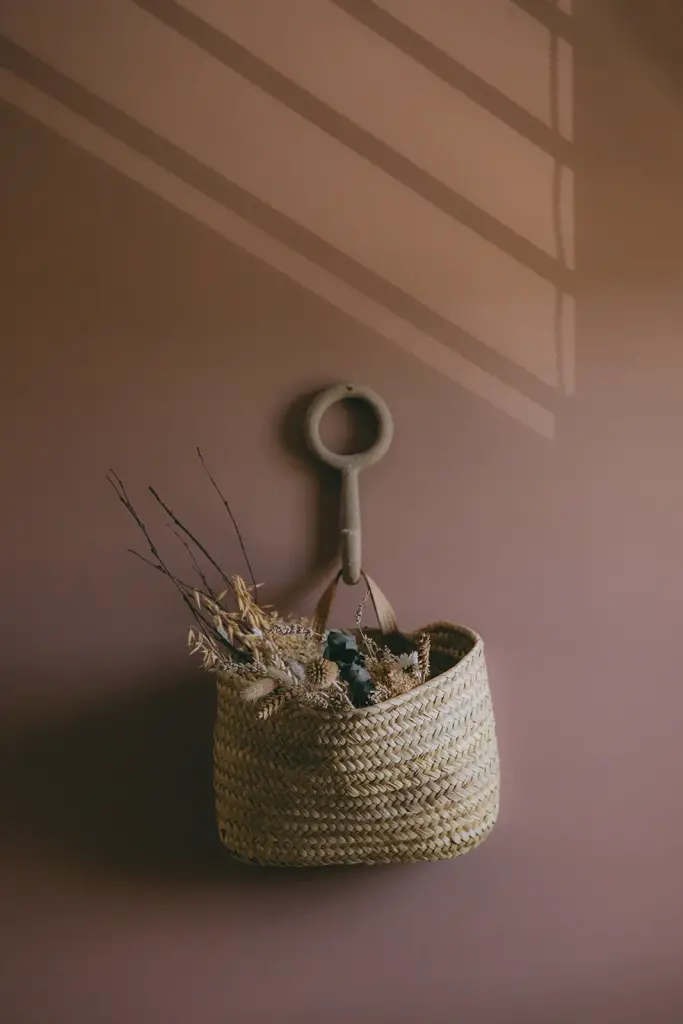 Panier en osier et fleurs séchées sur un mur terracotta, traversé par l’ombre d’une persienne