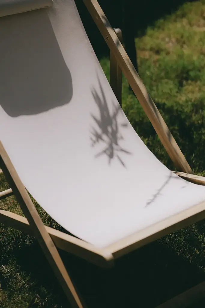 Transat en toile blanche dans l’herbe, l’ombre d’un feuillage posée dessus